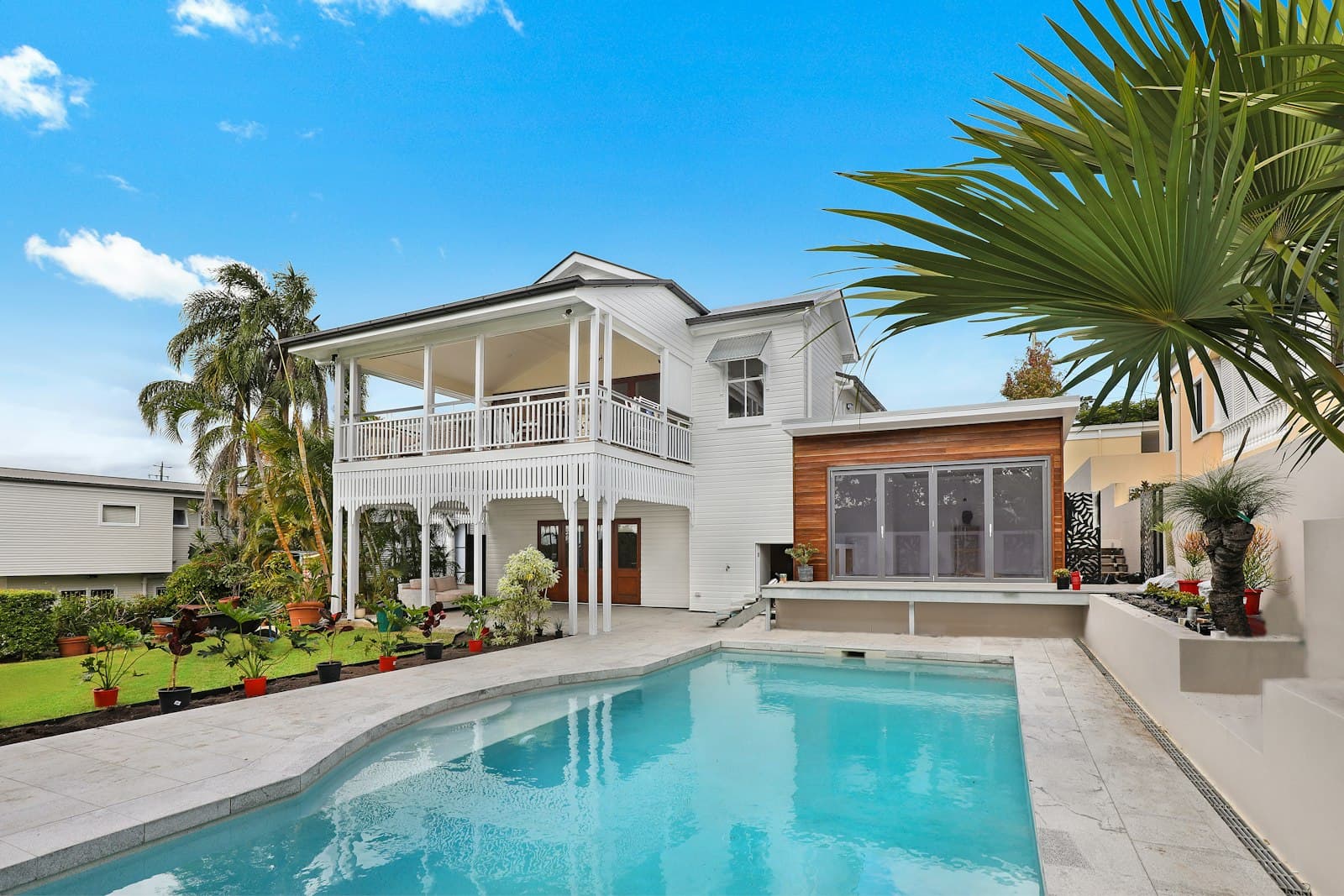 White two-story house with deep eaves, palm fronds, and a trimmed yard