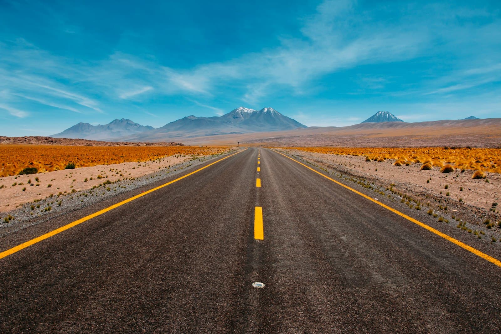 Empty two-lane highway running toward distant mountains under a blue sky