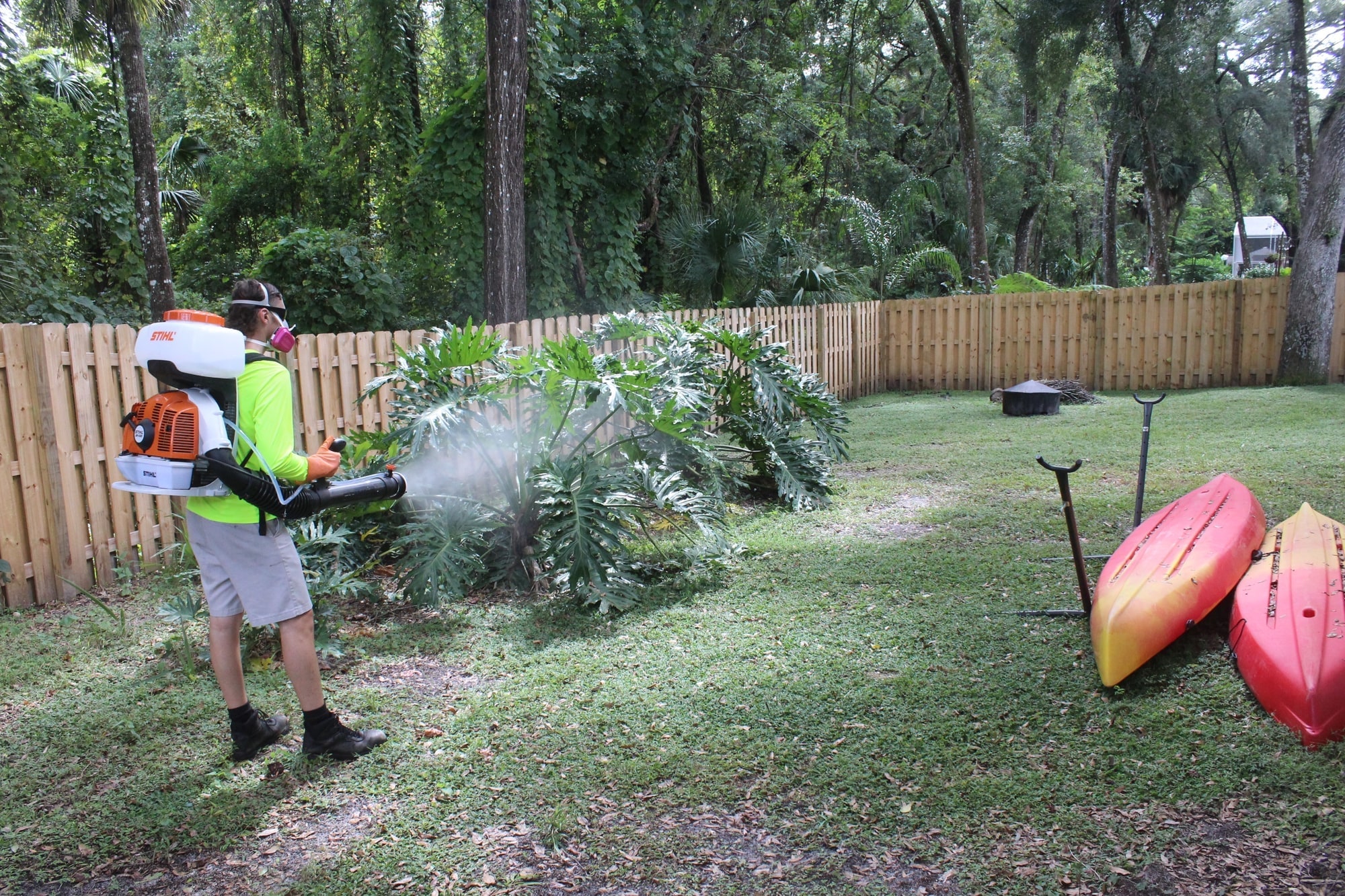 Technician applying barrier mosquito spray near landscaping